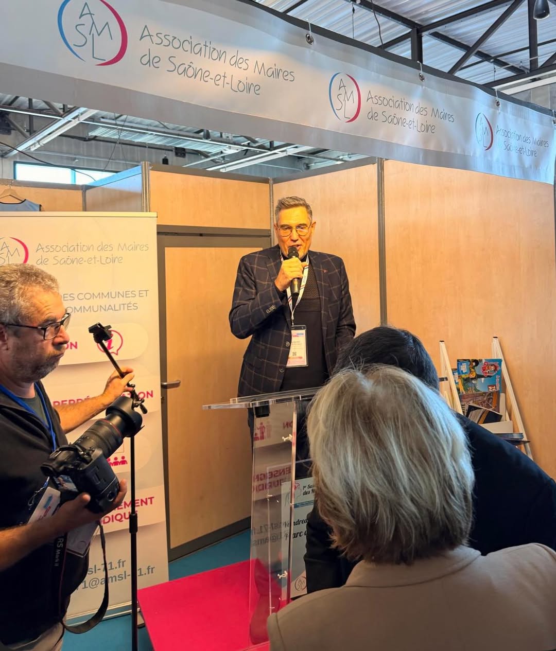 Un intervenant au micro, derrière le pupitre de l’Association des maires de Saône-et-Loire, lors de l’assemblée générale