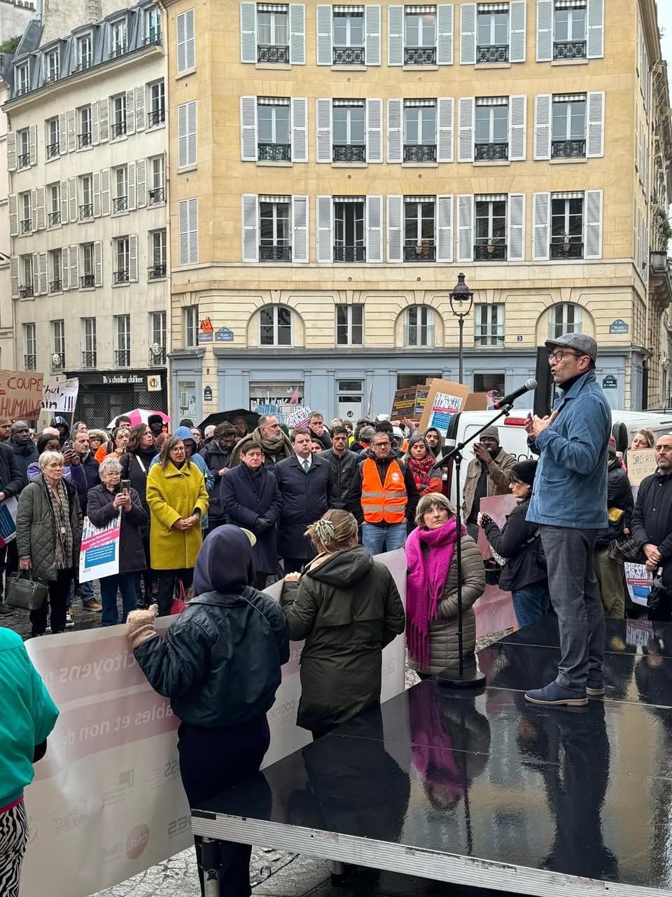 Rassemblement place de l’Odéon à Paris : un orateur au micro, sur une estrade, devant des manifestants et des pancartes