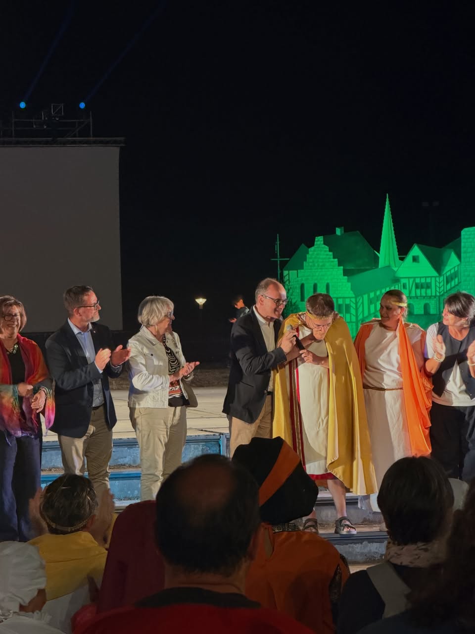 De nuit, sur la scène du théâtre romain d’Autun, Paulette Matray applaudit aux côtés d’élus et d’acteurs en costumes romains, devant un décor de ville illuminé en vert