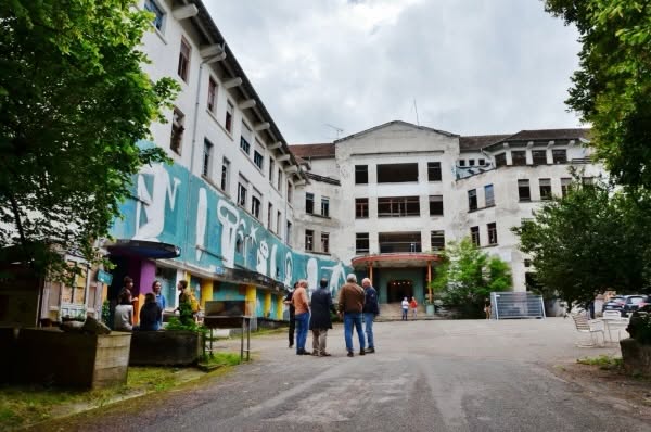 La façade de l’ancien sanatorium de Bergesserin, grand bâtiment blanc orné d’une fresque, devant lequel discutent quelques visiteurs