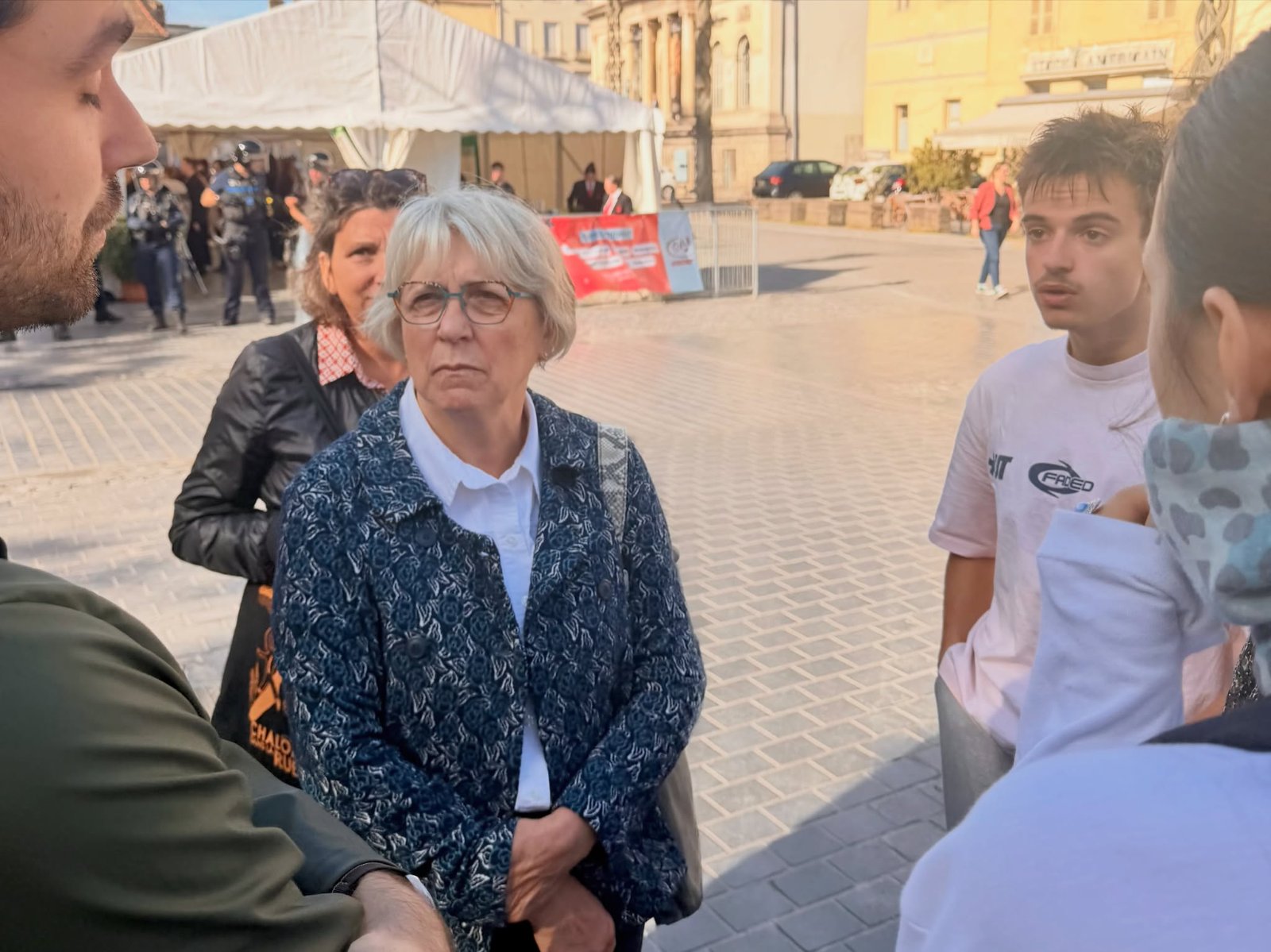 Paulette Matray, l’air grave, écoute des lycéens sur une place pavée de Chalon-sur-Saône