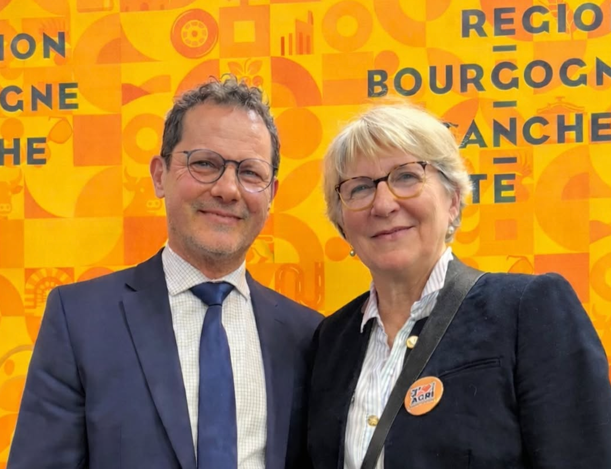 Paulette Matray et Jérôme Durain, souriants, devant le stand orange de la Région Bourgogne-Franche-Comté au Salon de l’agriculture