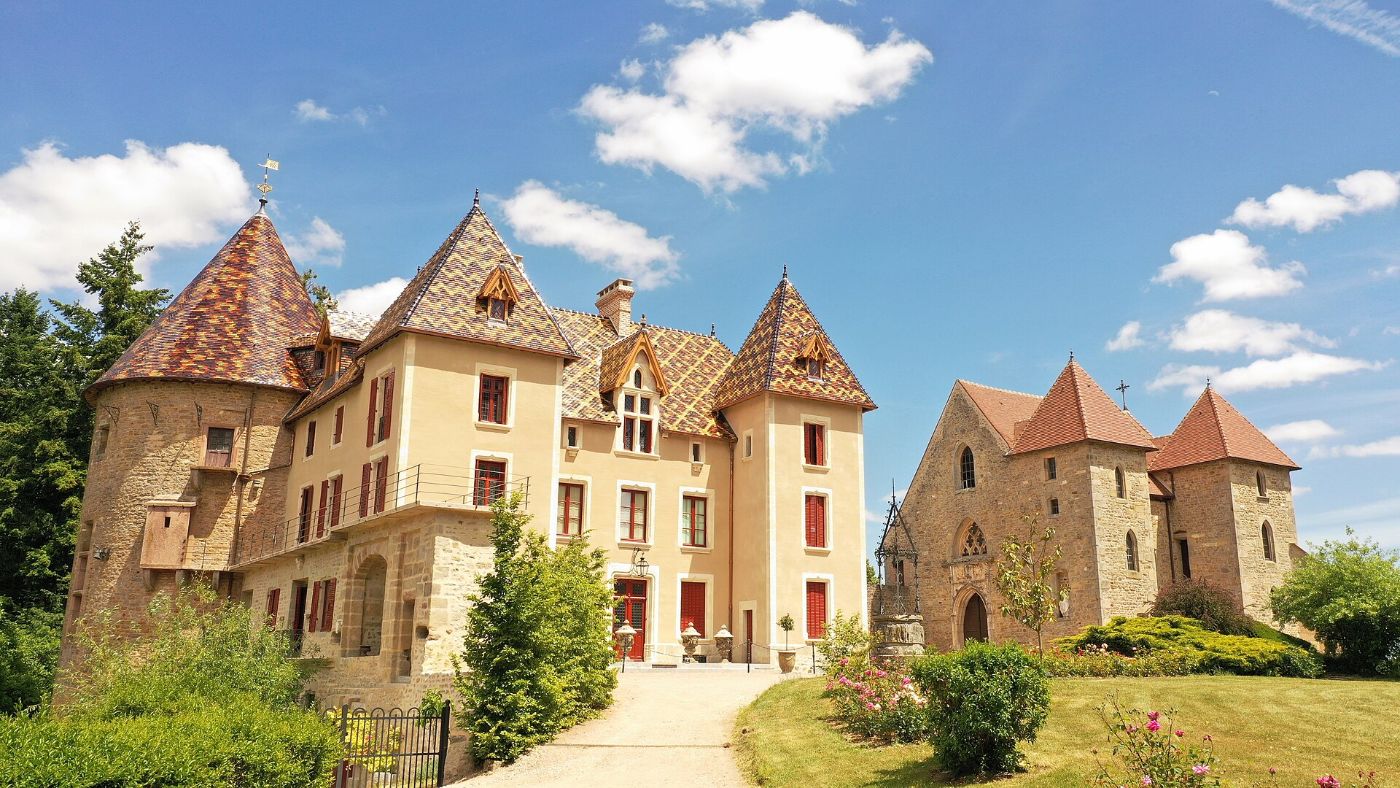 Le château de Couches, ses tours aux toits de tuiles vernissées et sa chapelle, au milieu d’un parc fleuri